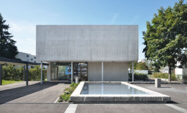 Die Kopfseite zeigt sich als monolithische Fläche in roh belassenem Sichtbeton.